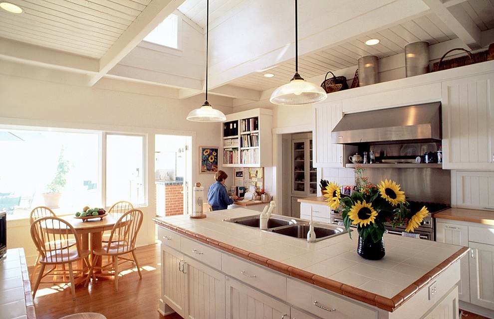 Photo of a beach style l-shaped separate kitchen in Santa Barbara with a double-bowl sink, shaker cabinets, white cabinets, wood benchtops, white splashback, ceramic splashback, medium hardwood floors and with island.