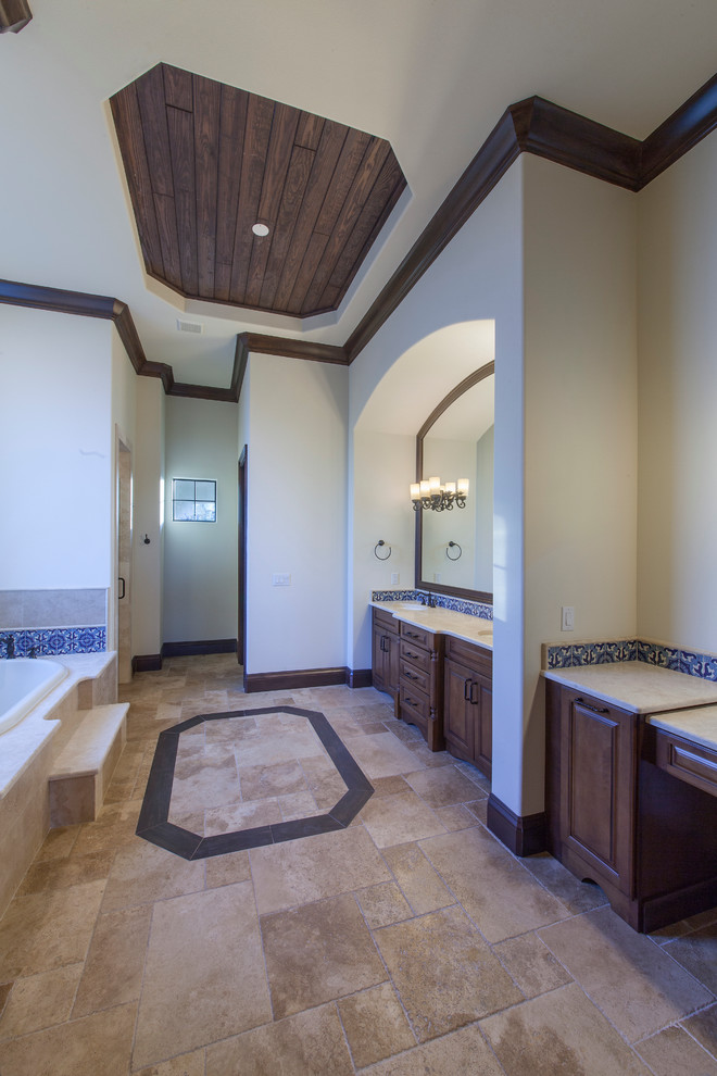 Expansive mediterranean master bathroom in Orlando with raised-panel cabinets, dark wood cabinets, a drop-in tub, a curbless shower, a one-piece toilet, blue tile, ceramic tile, beige walls, travertine floors, a drop-in sink and granite benchtops.