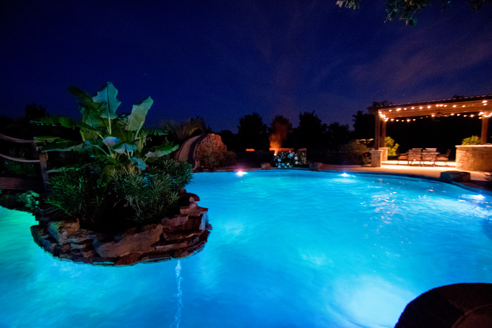 Expansive country backyard custom-shaped pool in Dallas with a water slide and natural stone pavers.