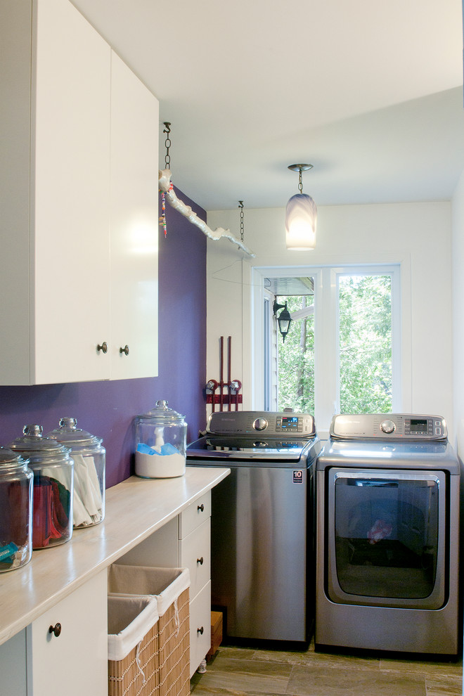 Design ideas for a mid-sized transitional galley utility room in Montreal with flat-panel cabinets, white cabinets, wood benchtops, purple walls, ceramic floors and a side-by-side washer and dryer.