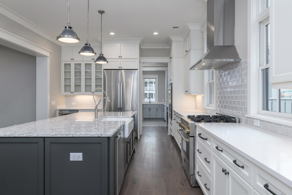 Inspiration for a transitional brown floor kitchen remodel with a farmhouse sink, gray backsplash, subway tile backsplash, stainless steel appliances, an island and white countertops