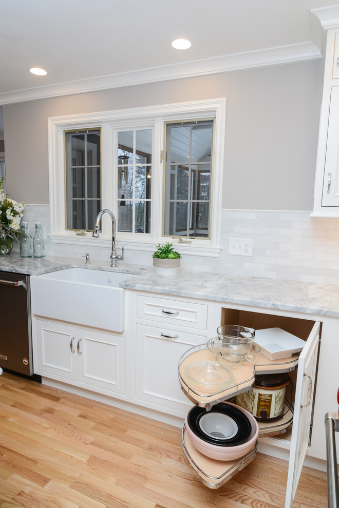 Large transitional u-shaped open plan kitchen in Boston with a farmhouse sink, beaded inset cabinets, white cabinets, granite benchtops, white splashback, marble splashback, stainless steel appliances, light hardwood floors, with island and white benchtop.