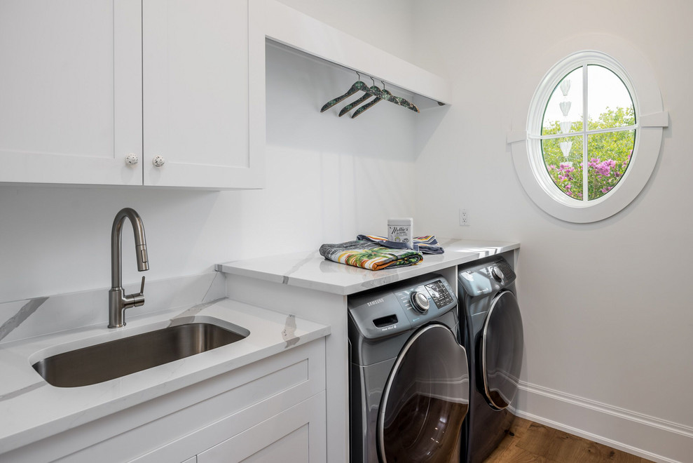 This is an example of a single-wall dedicated laundry room in Miami with an undermount sink, shaker cabinets, white cabinets, quartz benchtops, light hardwood floors, an integrated washer and dryer and white benchtop.