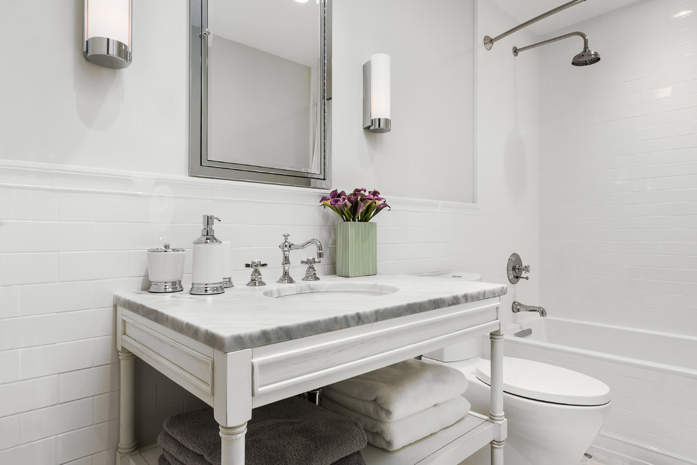 Alcove bathtub - transitional white tile and ceramic tile alcove bathtub idea in Los Angeles with an undermount sink, furniture-like cabinets, white cabinets, marble countertops and a two-piece toilet