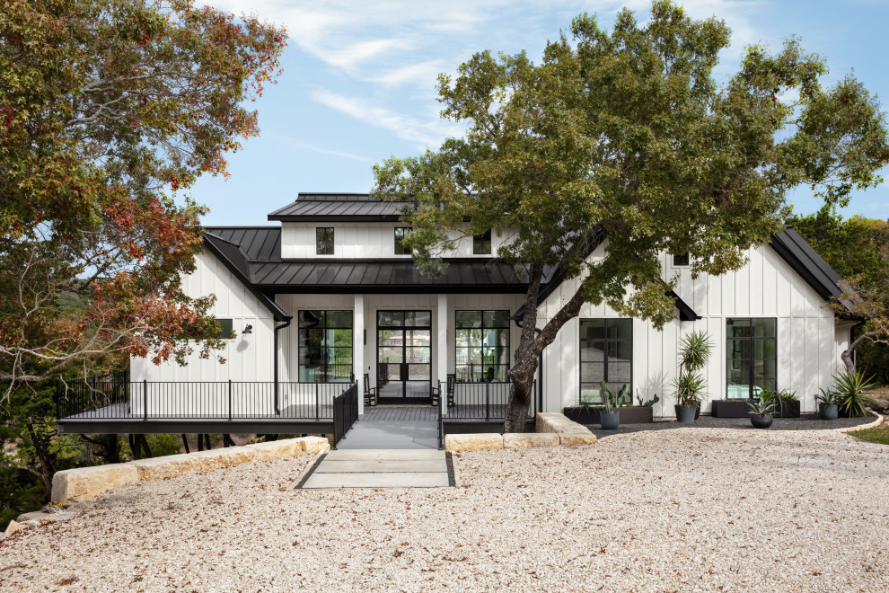 Photo of a mid-sized country one-storey white house exterior in Austin with wood siding, a shed roof, a metal roof, a black roof and board and batten siding.