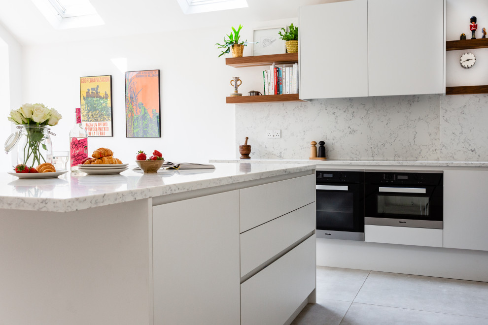 Inspiration for a mid-sized contemporary eat-in kitchen in London with a drop-in sink, flat-panel cabinets, white cabinets, marble benchtops, white splashback, marble splashback, black appliances, ceramic floors, with island, white floor and white benchtop.