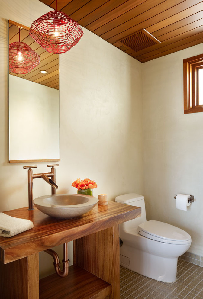 This is an example of a mid-sized tropical powder room in Los Angeles with a vessel sink, open cabinets, dark wood cabinets, beige walls, porcelain floors, wood benchtops, brown floor and brown benchtops.