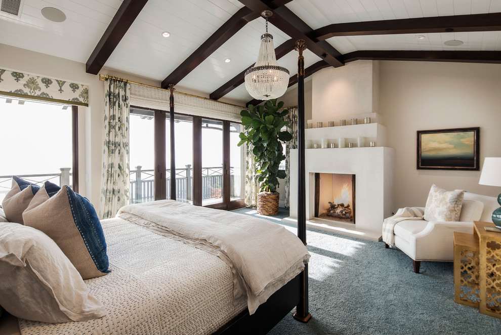 Photo of a large beach style master bedroom in Orange County with white walls, carpet, a standard fireplace and a plaster fireplace surround.