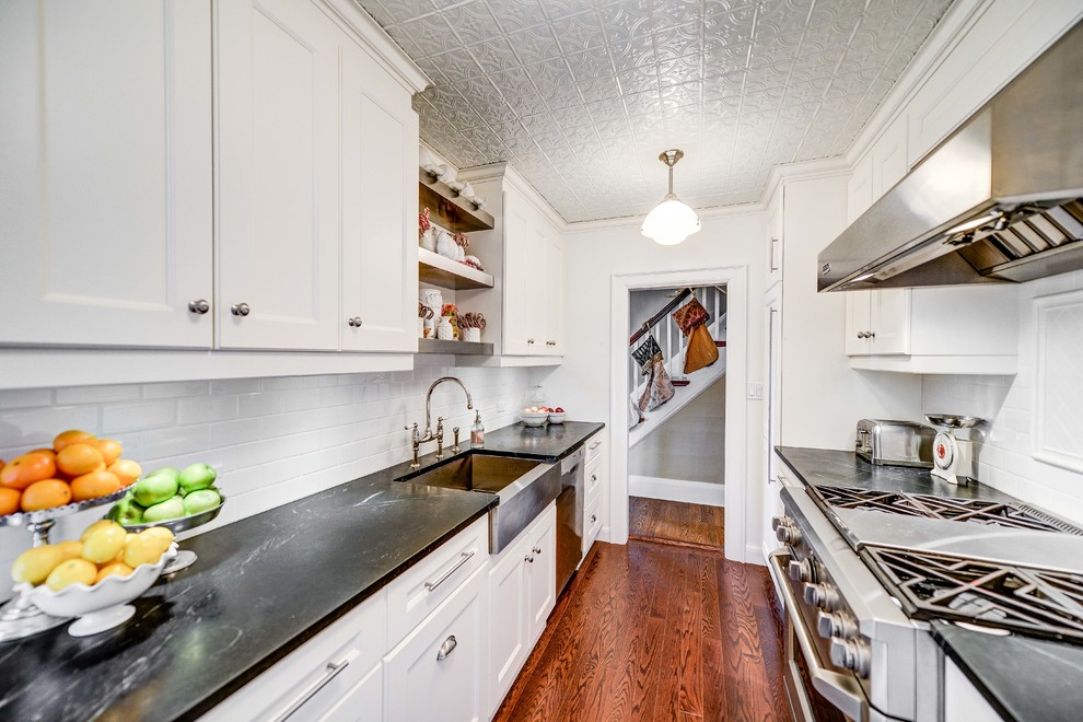 This is an example of a traditional galley separate kitchen in Toronto with a farmhouse sink, recessed-panel cabinets, white cabinets, soapstone benchtops, white splashback and subway tile splashback.