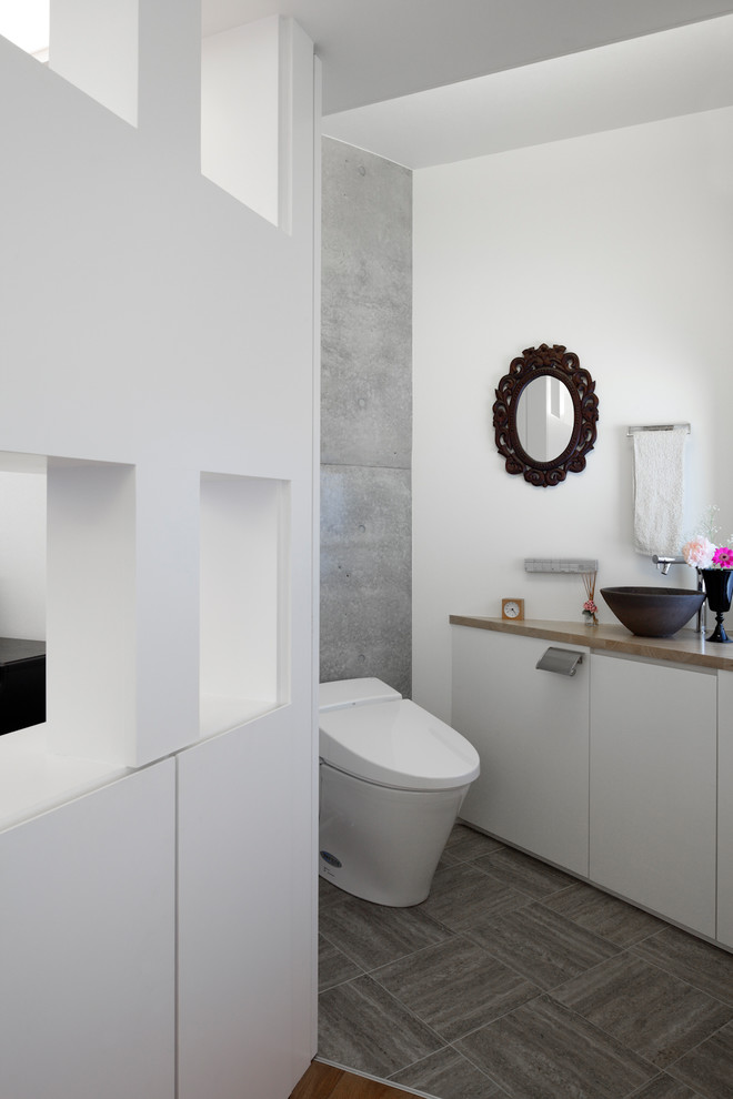 This is an example of a contemporary powder room in Tokyo Suburbs with an urinal, white walls, linoleum floors, a wall-mount sink, wood benchtops, grey floor, flat-panel cabinets and white cabinets.