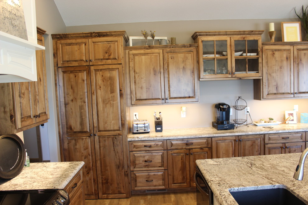 Open concept kitchen - large rustic l-shaped medium tone wood floor and brown floor open concept kitchen idea with an undermount sink, raised-panel cabinets, medium tone wood cabinets, granite countertops, stainless steel appliances and an island