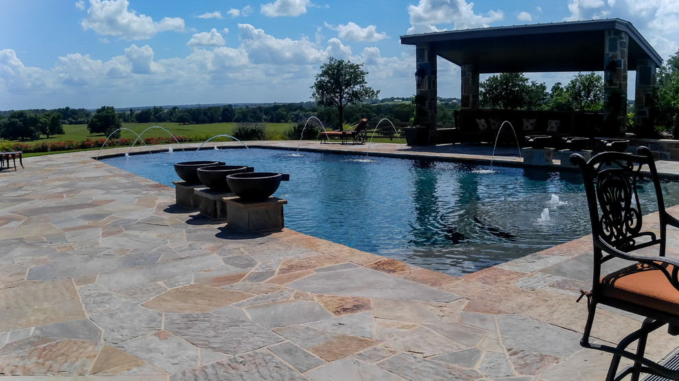 Photo of a large traditional backyard rectangular lap pool in Dallas with a water feature and natural stone pavers.