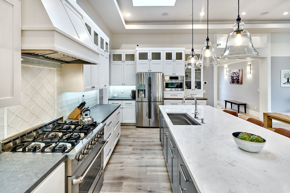 This is an example of a mid-sized transitional l-shaped open plan kitchen in San Francisco with an undermount sink, shaker cabinets, white cabinets, wood benchtops, grey splashback, glass tile splashback, stainless steel appliances, light hardwood floors and with island.