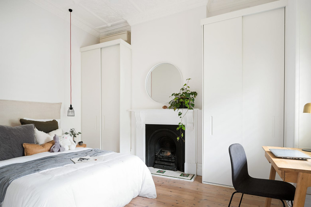 This is an example of a small modern guest bedroom in Sydney with white walls, light hardwood floors, a standard fireplace, a wood fireplace surround and grey floor.