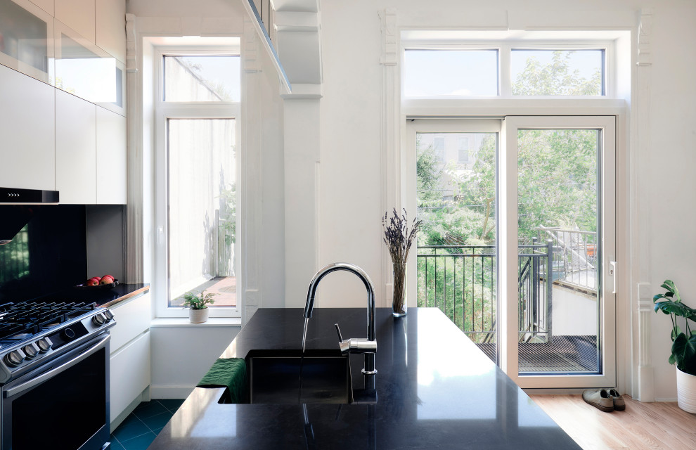 Exempel på ett mellanstort modernt svart linjärt svart kök och matrum, med en undermonterad diskho, släta luckor, vita skåp, granitbänkskiva, svart stänkskydd, rostfria vitvaror, klinkergolv i porslin, en köksö och grönt golv