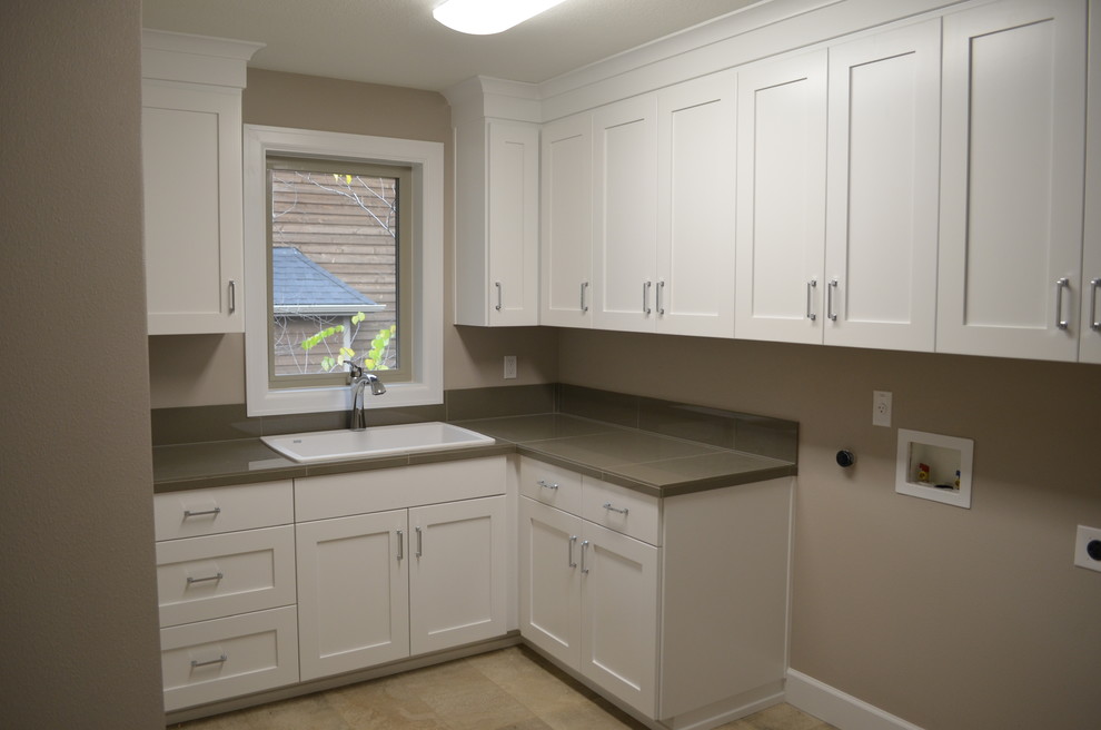 Inspiration for a large traditional l-shaped dedicated laundry room in Portland with a drop-in sink, shaker cabinets, white cabinets, tile benchtops, grey walls, travertine floors and a side-by-side washer and dryer.
