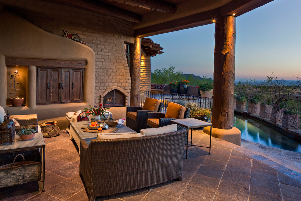 This is an example of a mid-sized backyard patio in Phoenix with a roof extension, natural stone pavers and with fireplace.
