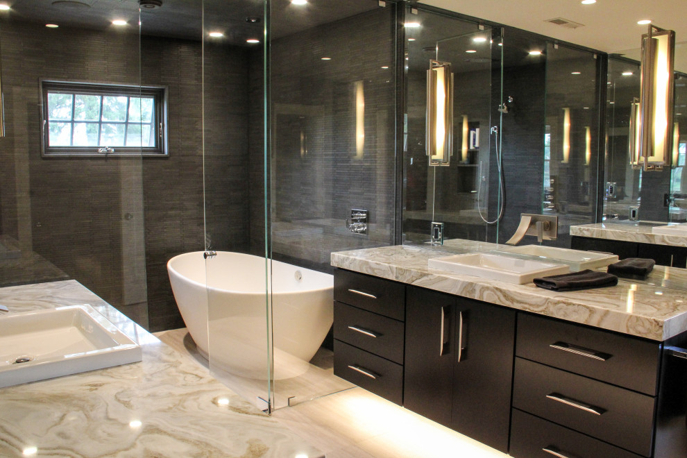 Photo of a mid-sized modern master wet room bathroom in Other with flat-panel cabinets, grey cabinets, a freestanding tub, black tile, stone tile, grey walls, limestone floors, a drop-in sink, granite benchtops, a hinged shower door, an enclosed toilet, a double vanity and a floating vanity.