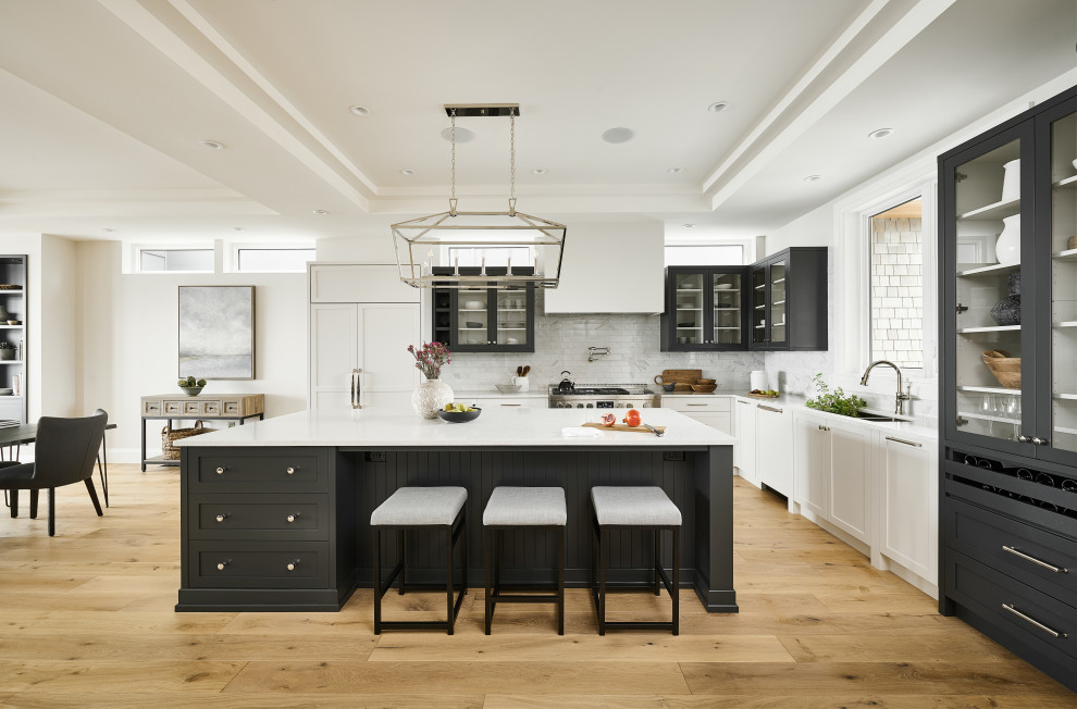 Large transitional l-shaped medium tone wood floor, brown floor and tray ceiling kitchen photo with an undermount sink, shaker cabinets, quartzite countertops, white backsplash, subway tile backsplash, paneled appliances, an island, white countertops and white cabinets