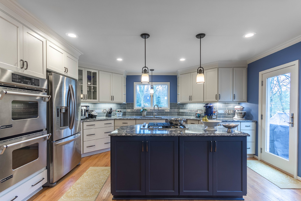 Photo of a large transitional u-shaped eat-in kitchen in Detroit with an undermount sink, flat-panel cabinets, quartz benchtops, blue splashback, glass tile splashback, stainless steel appliances, light hardwood floors, with island, brown floor and grey cabinets.