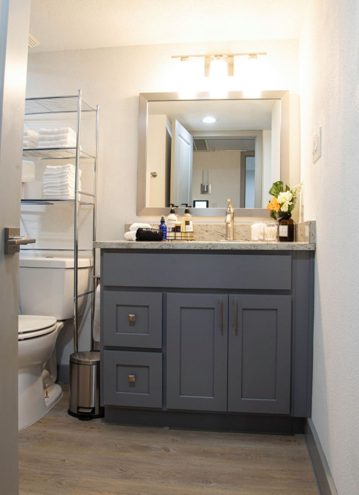 This is an example of a small contemporary master bathroom in Houston with flat-panel cabinets, grey cabinets, a drop-in tub, a shower/bathtub combo, a one-piece toilet, white tile, ceramic tile, white walls, medium hardwood floors, granite benchtops, brown floor, a shower curtain, beige benchtops, a shower seat, a single vanity and a built-in vanity.