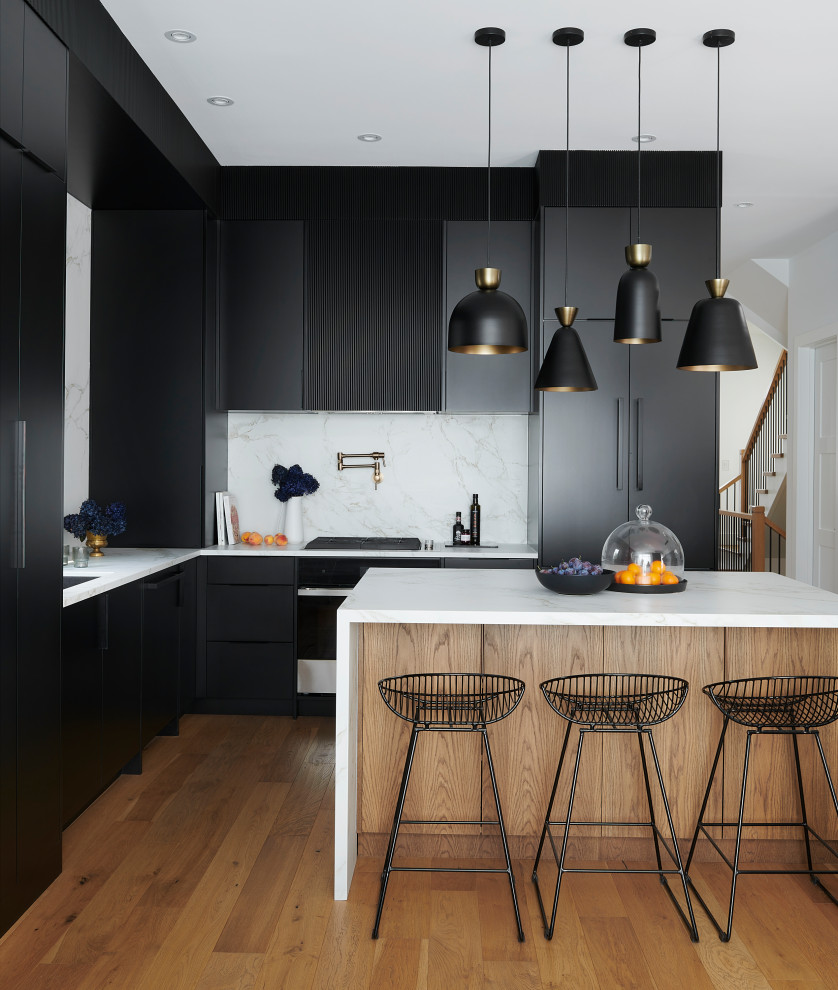 Mid-sized contemporary l-shaped open plan kitchen in Toronto with a double-bowl sink, flat-panel cabinets, black cabinets, quartz benchtops, white splashback, porcelain splashback, panelled appliances, light hardwood floors, with island and white benchtop.