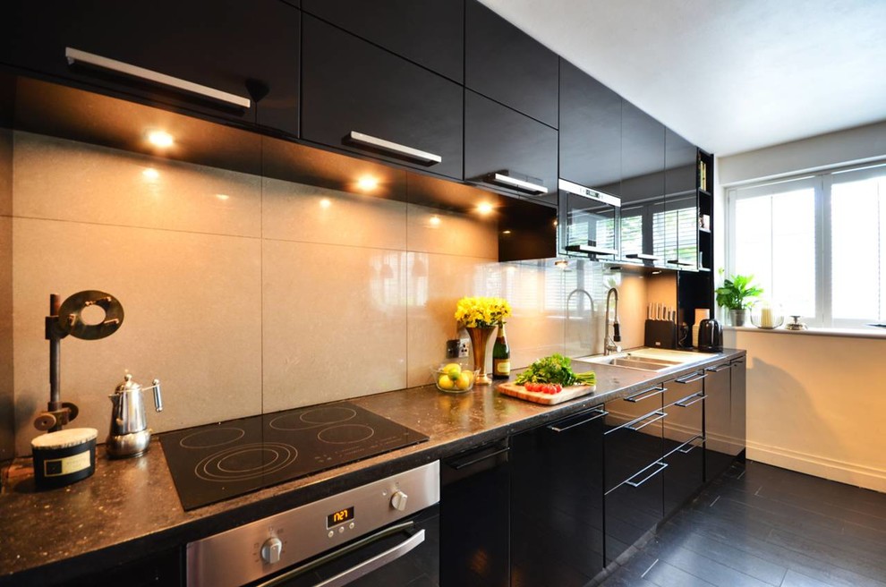 Photo of a small modern galley open plan kitchen in London with a drop-in sink, flat-panel cabinets, black cabinets, concrete benchtops, grey splashback, porcelain splashback, panelled appliances and bamboo floors.