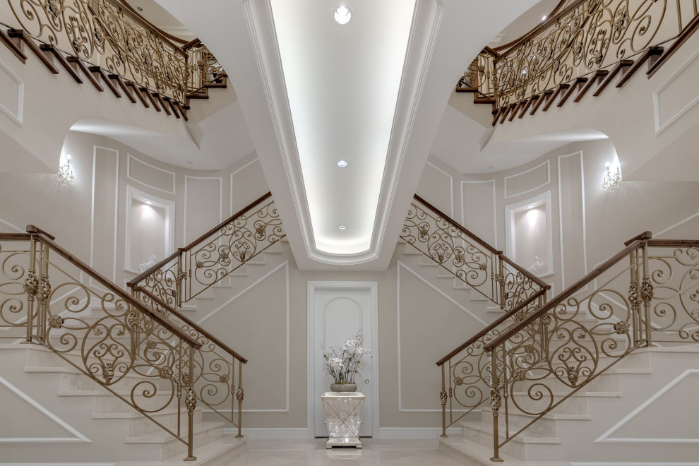 Imagen de escalera en L clásica grande con escalones de mármol, contrahuellas de mármol, barandilla de metal y panelado
