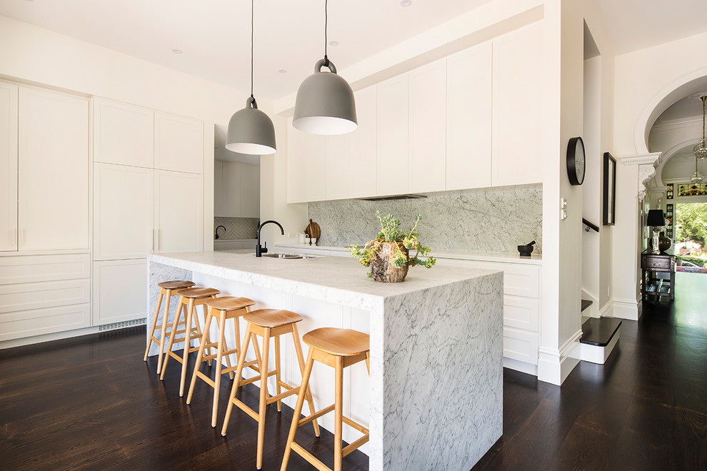 Inspiration for a contemporary galley open plan kitchen in Melbourne with a double-bowl sink, shaker cabinets, white cabinets, grey splashback, marble splashback, dark hardwood floors, with island and brown floor.