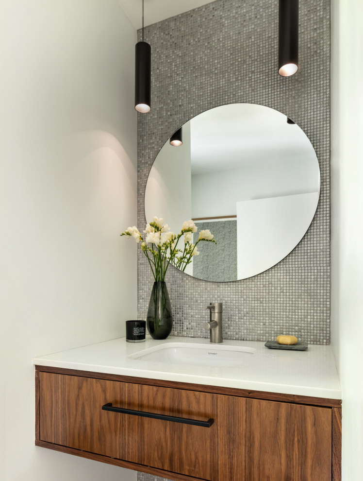 Photo of a mid-sized contemporary bathroom in New York with furniture-like cabinets, brown cabinets, a one-piece toilet, metal tile, white walls, porcelain floors, an undermount sink, grey floor, white benchtops, a single vanity and a floating vanity.