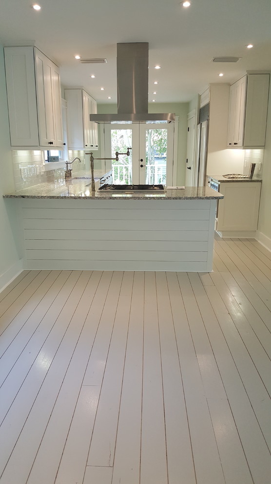 Photo of a beach style galley eat-in kitchen in Jacksonville with a farmhouse sink, shaker cabinets, white cabinets, white splashback, glass tile splashback, stainless steel appliances, painted wood floors and grey floor.