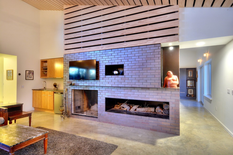Photo of a mid-sized modern open concept living room in Austin with a home bar, white walls, concrete floors, a standard fireplace, a brick fireplace surround and a wall-mounted tv.