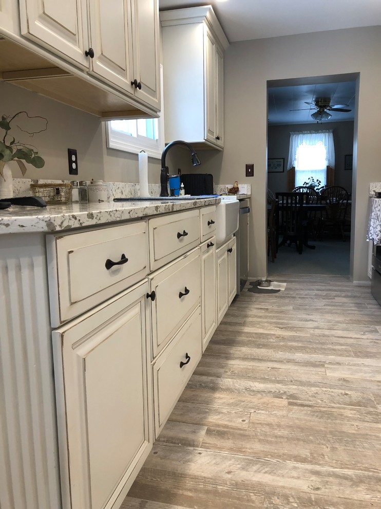 This is an example of a small traditional galley separate kitchen in Burlington with a farmhouse sink, raised-panel cabinets, distressed cabinets, stainless steel appliances, no island, grey floor and white benchtop.