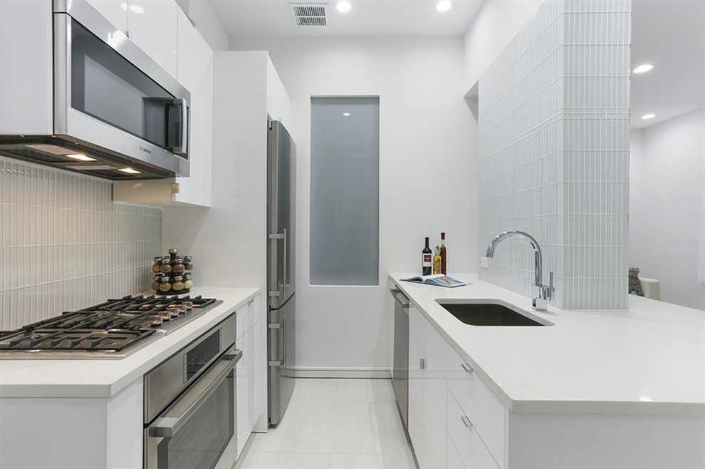 Photo of a small modern galley eat-in kitchen in New York with an undermount sink, flat-panel cabinets, white cabinets, glass tile splashback, stainless steel appliances, no island, quartz benchtops, white floor, white splashback, porcelain floors and white benchtop.
