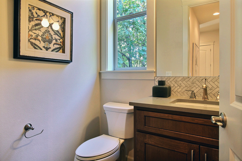 This is an example of a mid-sized arts and crafts powder room in Portland with recessed-panel cabinets, dark wood cabinets, a two-piece toilet, black and white tile, ceramic tile, white walls, ceramic floors, an undermount sink, engineered quartz benchtops, white floor and grey benchtops.