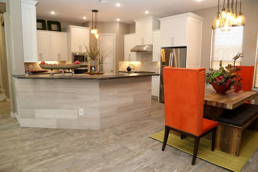 Example of a small transitional u-shaped light wood floor eat-in kitchen design in Orange County with an undermount sink, louvered cabinets, white cabinets, solid surface countertops, beige backsplash, stone tile backsplash, stainless steel appliances and two islands