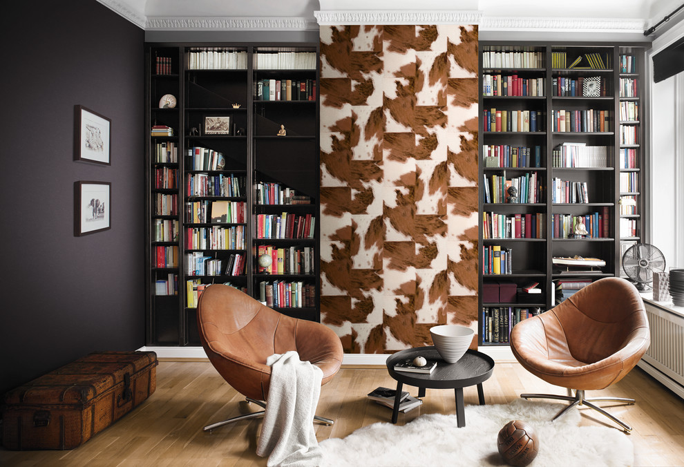 This is an example of a transitional living room in New York with a library, black walls and light hardwood floors.