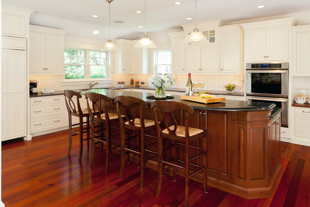 Transitional l-shaped medium tone wood floor eat-in kitchen photo in Boston with an undermount sink, raised-panel cabinets, white cabinets, granite countertops, white backsplash, ceramic backsplash, stainless steel appliances and an island