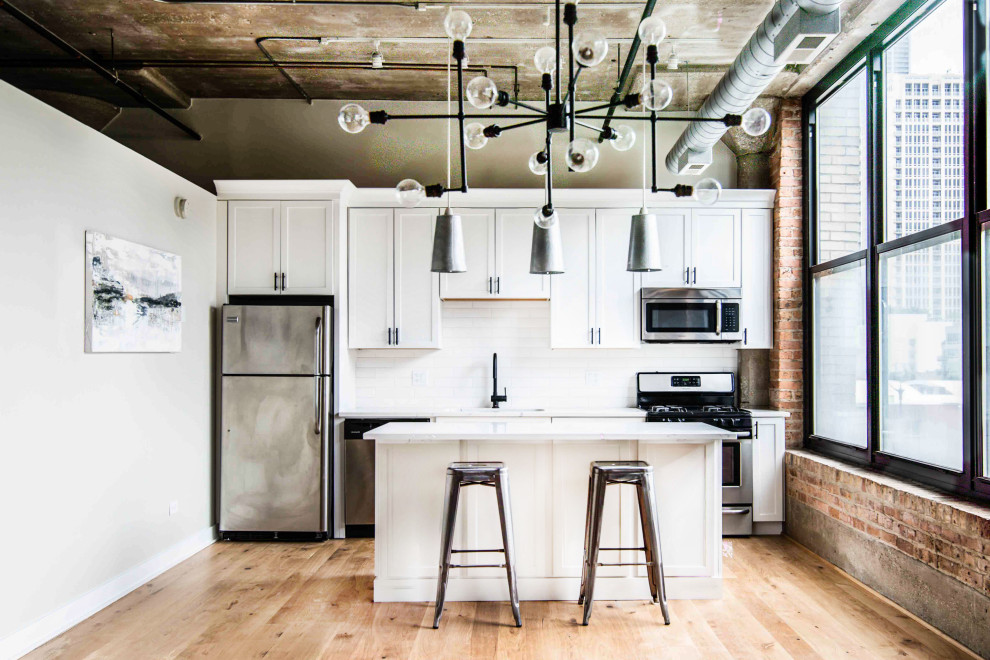 Inspiration for an urban single-wall kitchen/diner in Chicago with a submerged sink, recessed-panel cabinets, white cabinets, quartz worktops, white splashback, ceramic splashback, stainless steel appliances, light hardwood flooring, an island and white worktops.