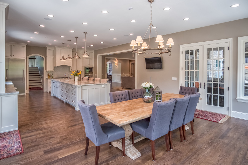 Example of a large transitional l-shaped medium tone wood floor eat-in kitchen design with a farmhouse sink, shaker cabinets, white cabinets, marble countertops, white backsplash, subway tile backsplash, stainless steel appliances and an island