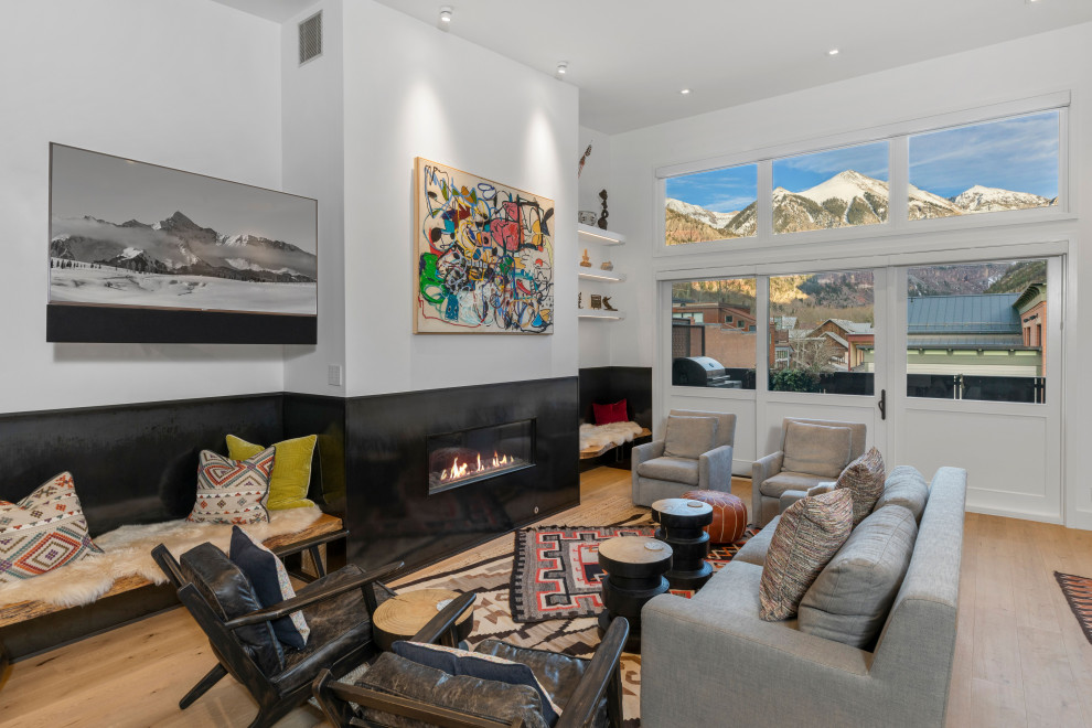 This is an example of a contemporary open plan games room in Denver with white walls, light hardwood flooring, a ribbon fireplace, a wall mounted tv, beige floors and a chimney breast.