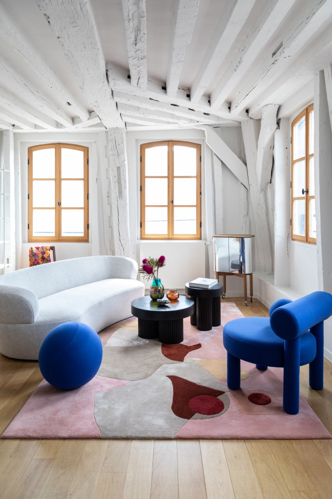 Modelo de salón abierto contemporáneo de tamaño medio sin chimenea y televisor con paredes blancas, suelo de madera clara, suelo beige y vigas vistas