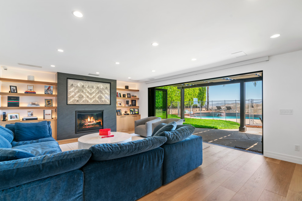Inspiration for a large contemporary open plan games room in Los Angeles with white walls, light hardwood flooring, a standard fireplace, a wall mounted tv and beige floors.