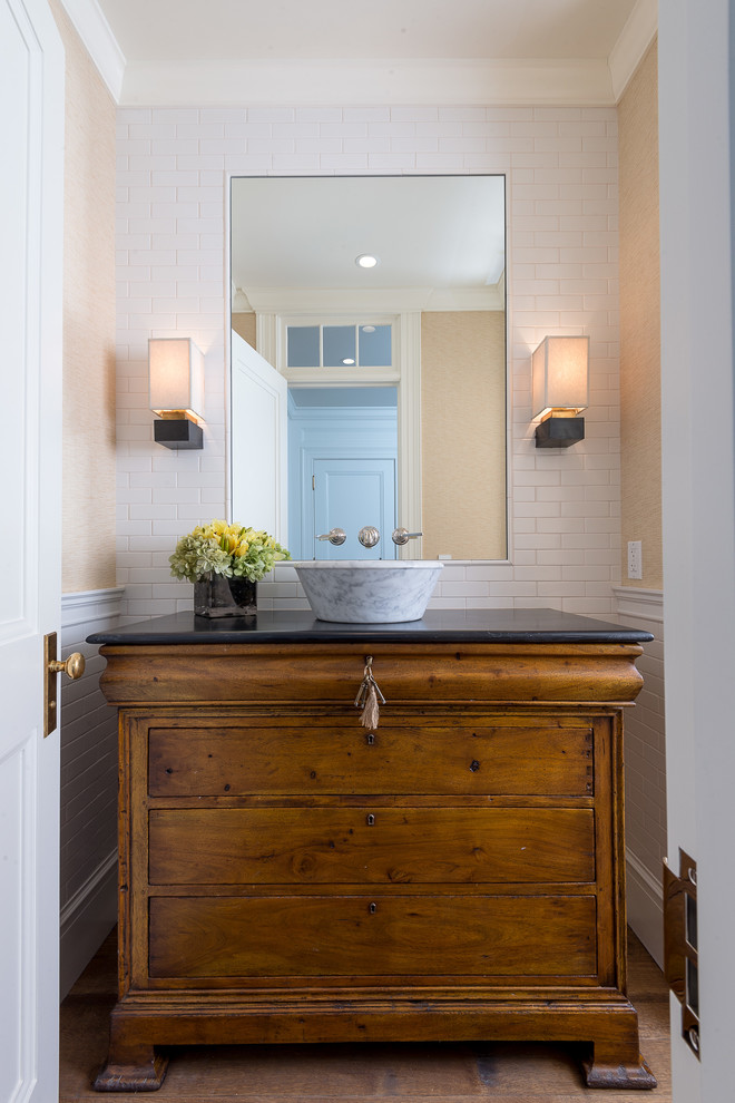 Inspiration for a traditional powder room in Los Angeles with furniture-like cabinets, a vessel sink, medium wood cabinets, white tile, beige walls and black benchtops.
