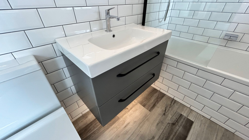 Photo of a small modern kids bathroom in Hampshire with flat-panel cabinets, grey cabinets, a drop-in tub, a shower/bathtub combo, a two-piece toilet, black and white tile, porcelain tile, white walls, vinyl floors, an integrated sink, grey floor, a hinged shower door, a laundry, a single vanity and a floating vanity.