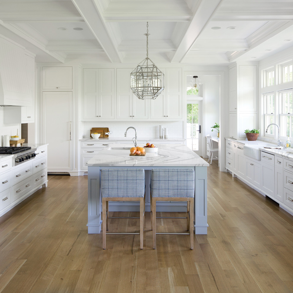 Large beach style u-shaped kitchen in Minneapolis with quartz benchtops, with island, a farmhouse sink, recessed-panel cabinets, white cabinets, white splashback, panelled appliances, medium hardwood floors and brown floor.