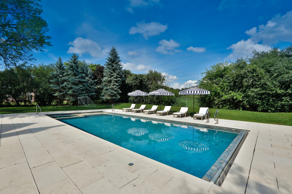 This is an example of a mid-sized traditional backyard rectangular lap pool in Chicago with a hot tub and natural stone pavers.