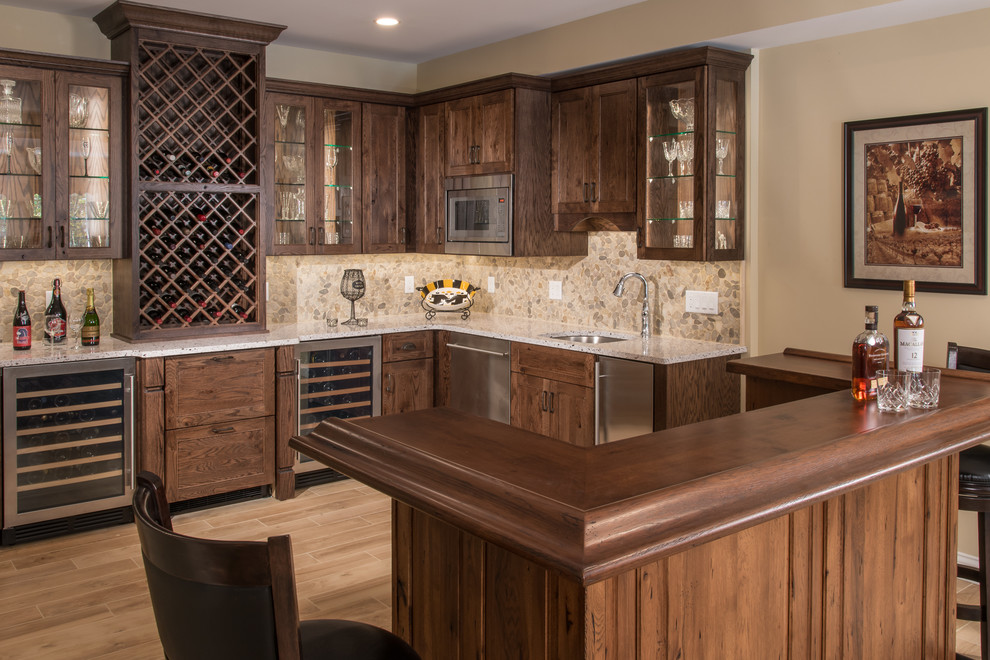 Inspiration for a traditional l-shaped seated home bar in St Louis with an undermount sink, raised-panel cabinets, distressed cabinets, solid surface benchtops, multi-coloured splashback, stone tile splashback and porcelain floors.