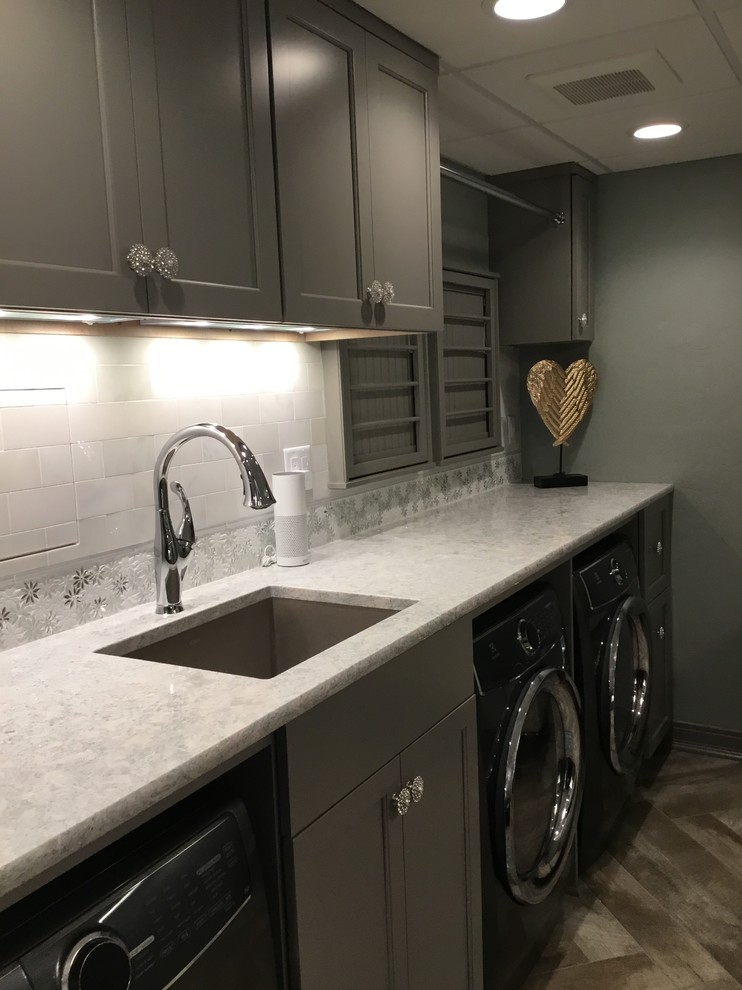 Large traditional utility room in Milwaukee with an undermount sink, recessed-panel cabinets, grey cabinets, quartz benchtops, vinyl floors, a side-by-side washer and dryer, brown floor and white benchtop.