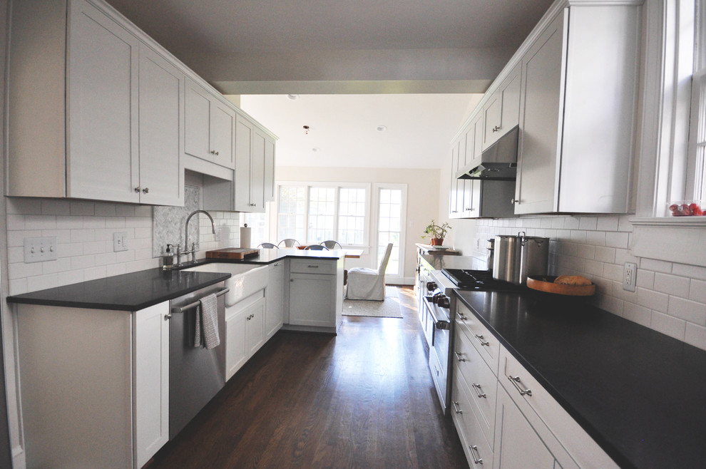 Example of a mid-sized transitional galley medium tone wood floor and brown floor eat-in kitchen design in Richmond with a farmhouse sink, shaker cabinets, white cabinets, granite countertops, white backsplash, subway tile backsplash, stainless steel appliances and a peninsula